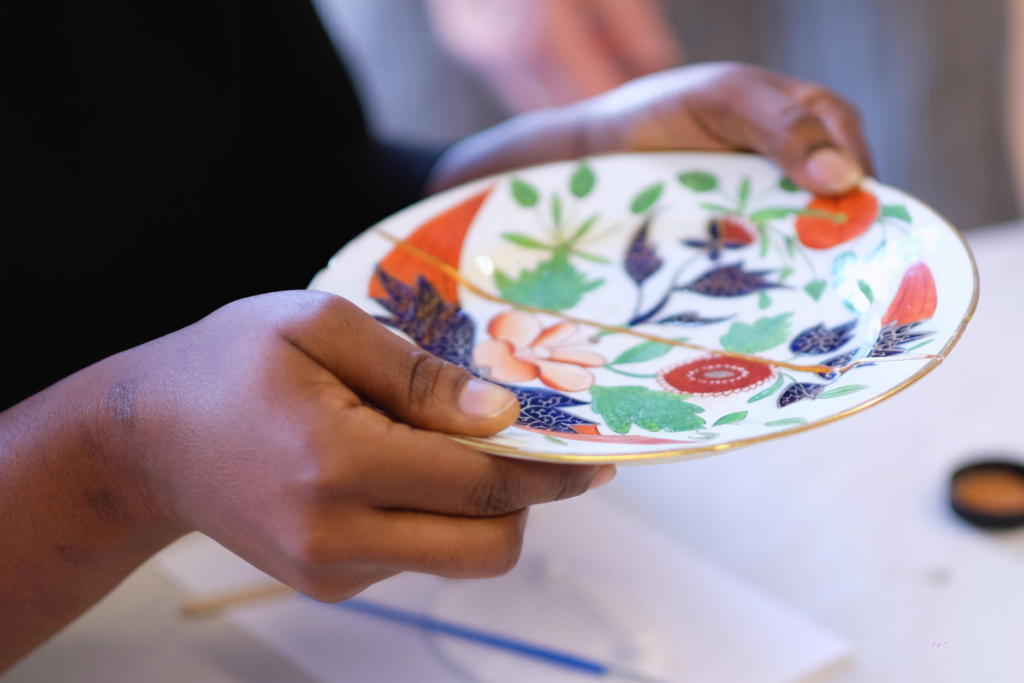 A picture of hands holding together two pieces of an antique ceramic plate which is being repaired with the kintsugi technique.